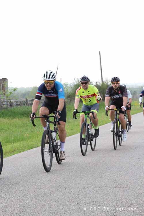 Vigilant cyclists riding on scenic rural road during Bluebonnet Express event.