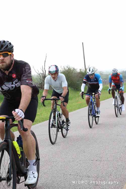 - Diverse group of cyclists riding on scenic rural road in Bluebonnet Express cycling event.