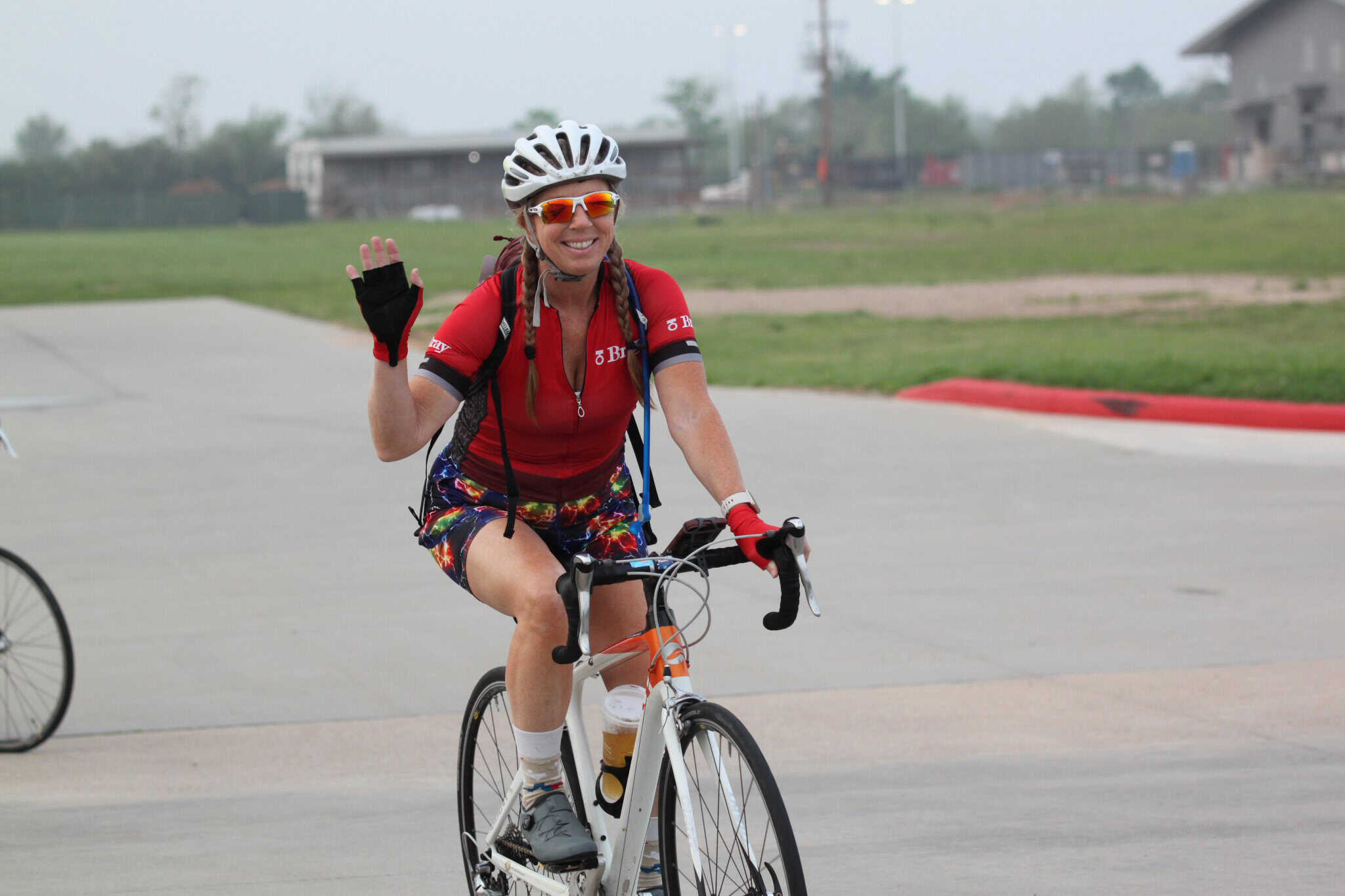 Vibrant female cyclist waving while riding on a scenic bike trail with Bluebonnet Express branding.