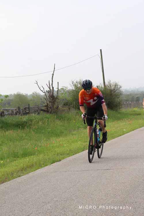 Cyclist riding on scenic rural road with greenery and overcast sky for Bluebonnet Express event.