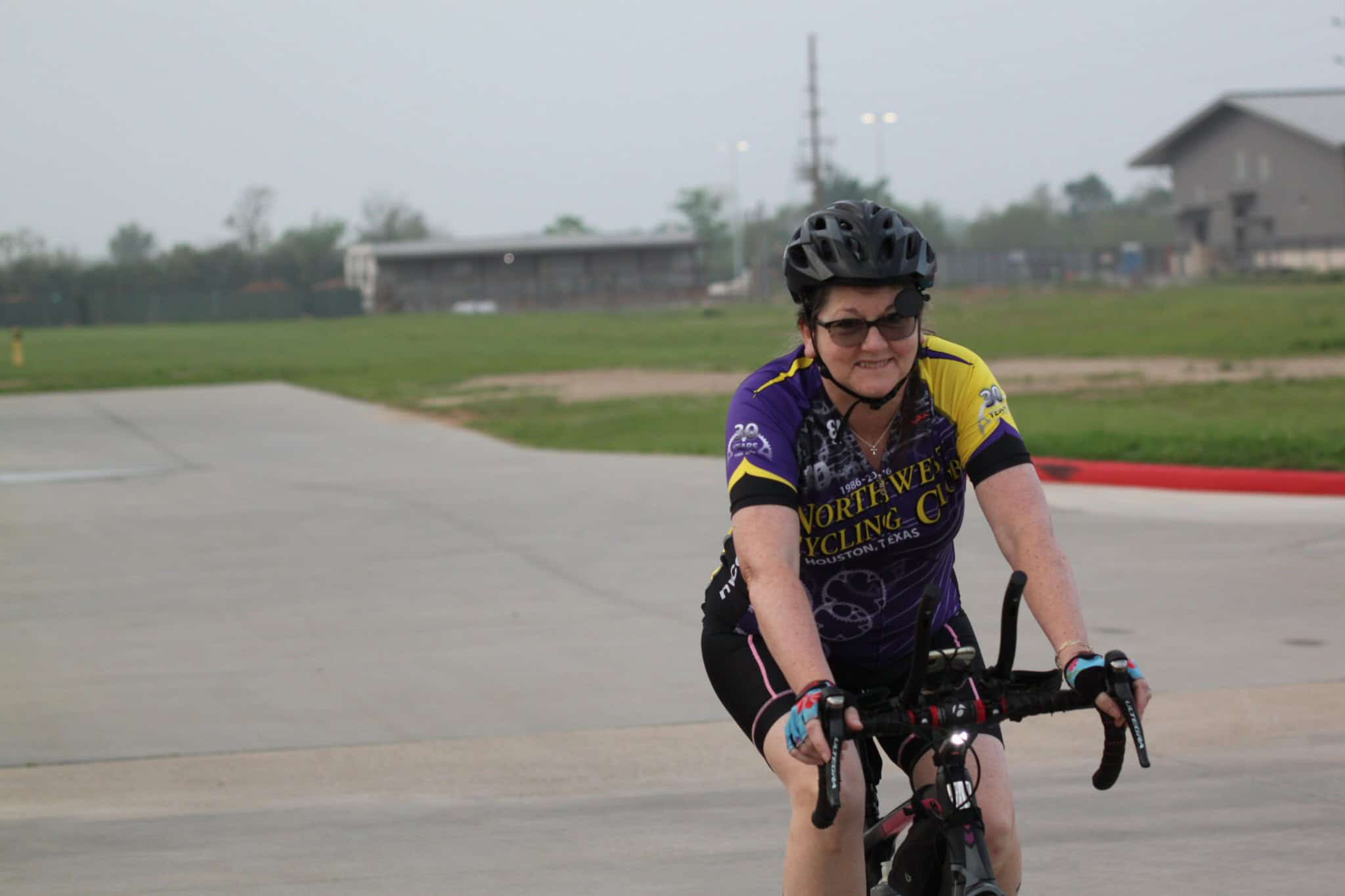 Smiling woman riding a bicycle at Bluebonnet Express cycling event, Houston Texas, wearing a purple cycling jersey.