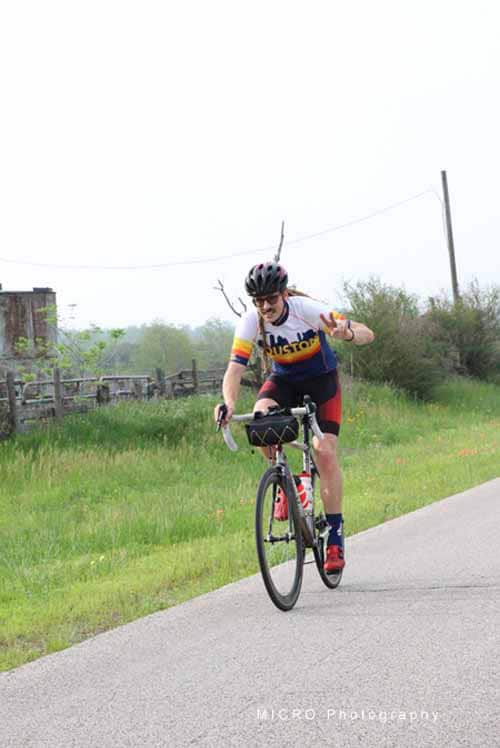 Bright female cyclist riding a bike on rural road during daytime, promoting Bluebonnet Express cycling tour.
