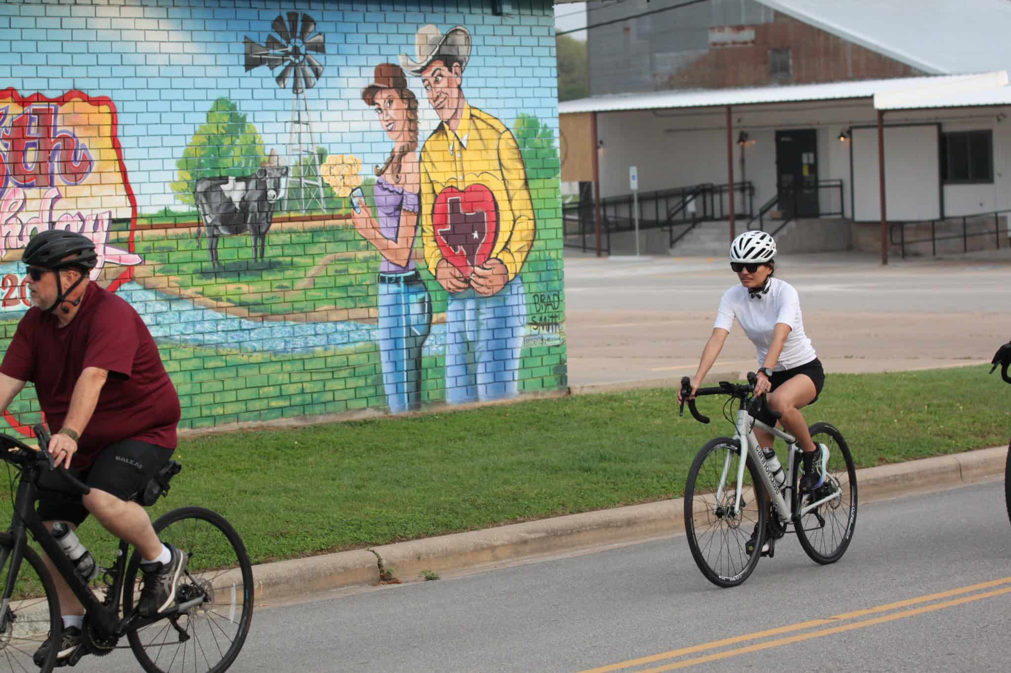Colorful mural of farmers and farm animals along with cyclists riding on a city street.