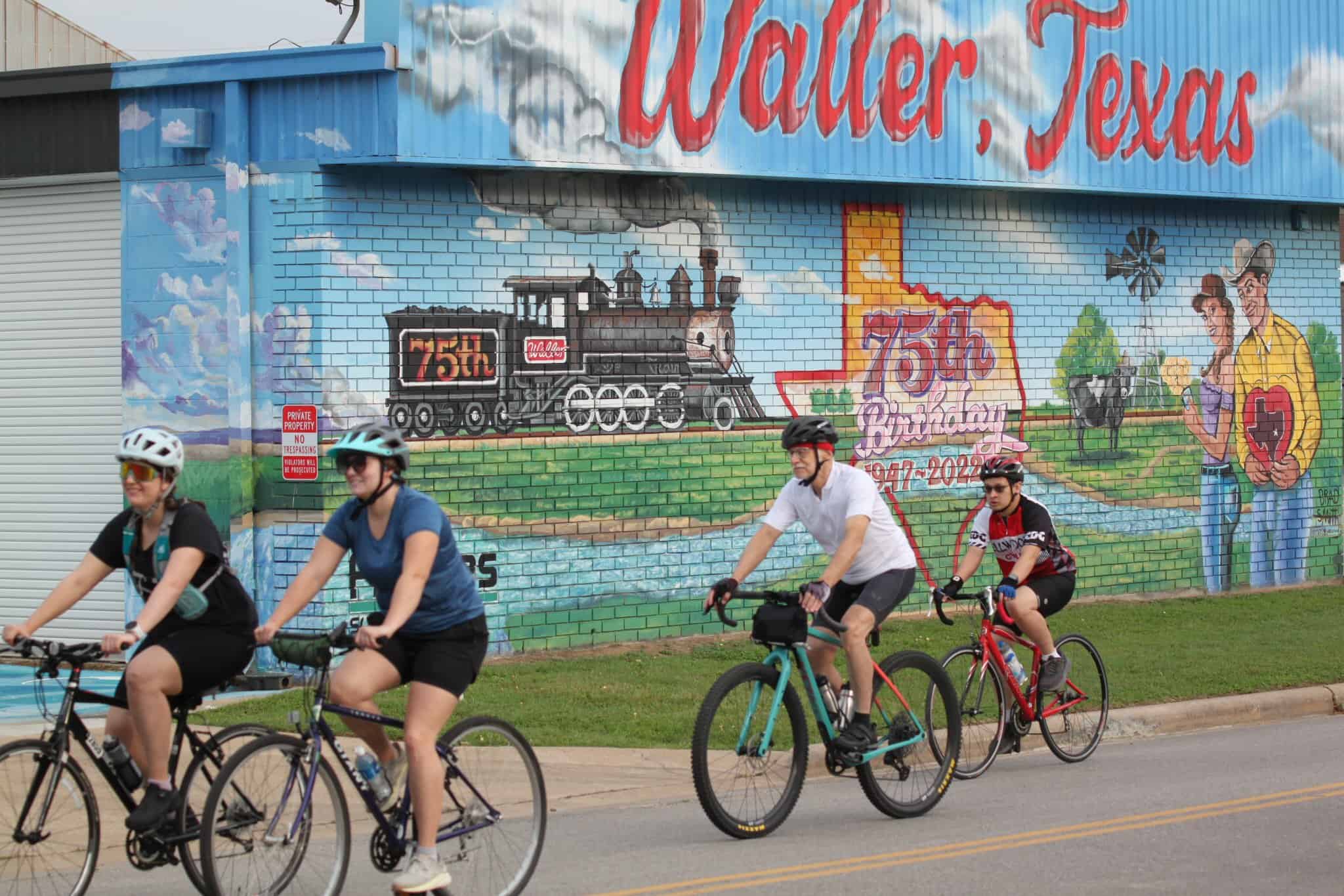 Colorful mural celebrating Waller, Texas 75th birthday with cyclists riding past.