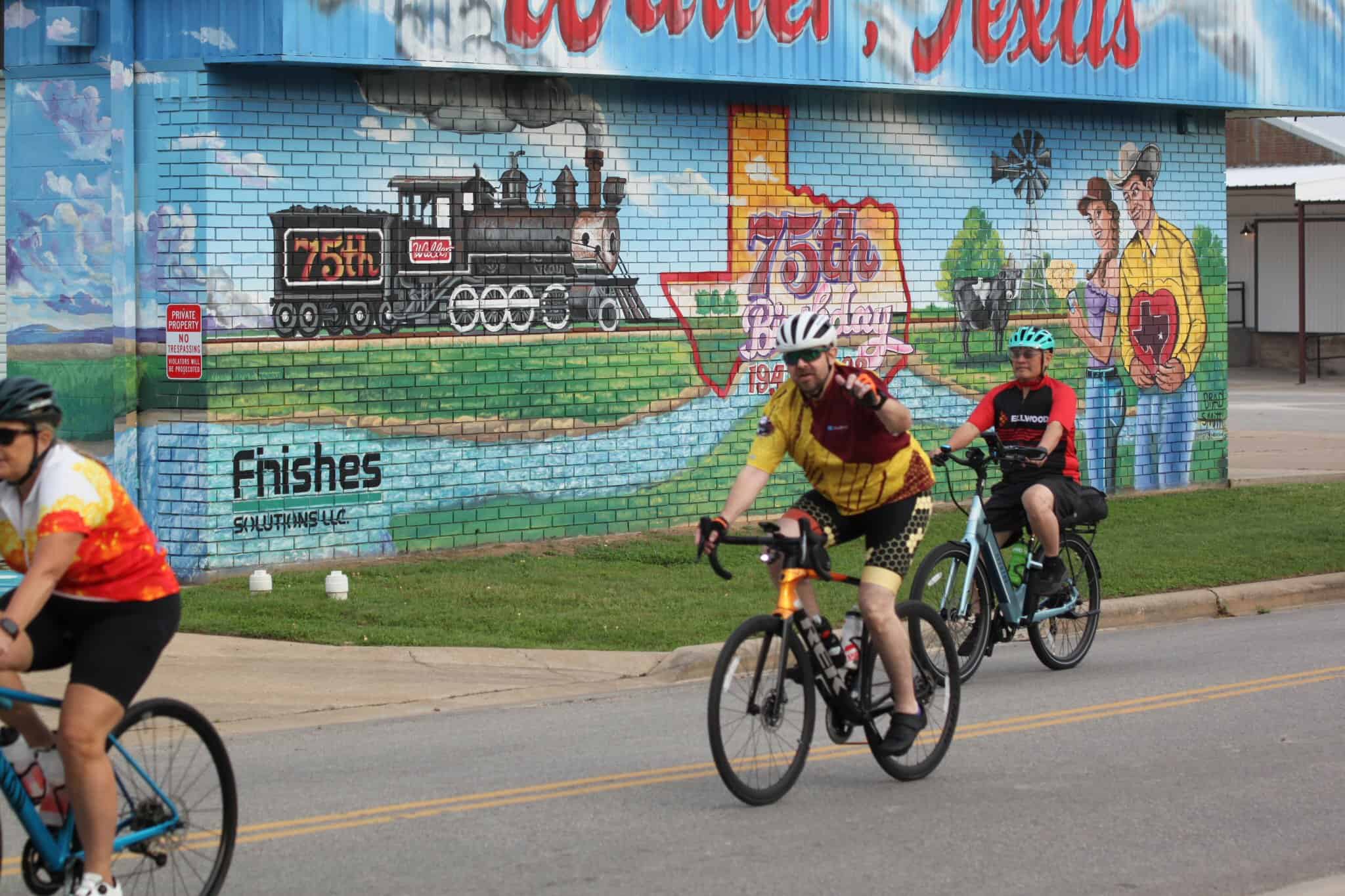Colorful mural celebrating 75th anniversary along with cyclists riding on street, highlighting Bluebonnet Express bike tour.