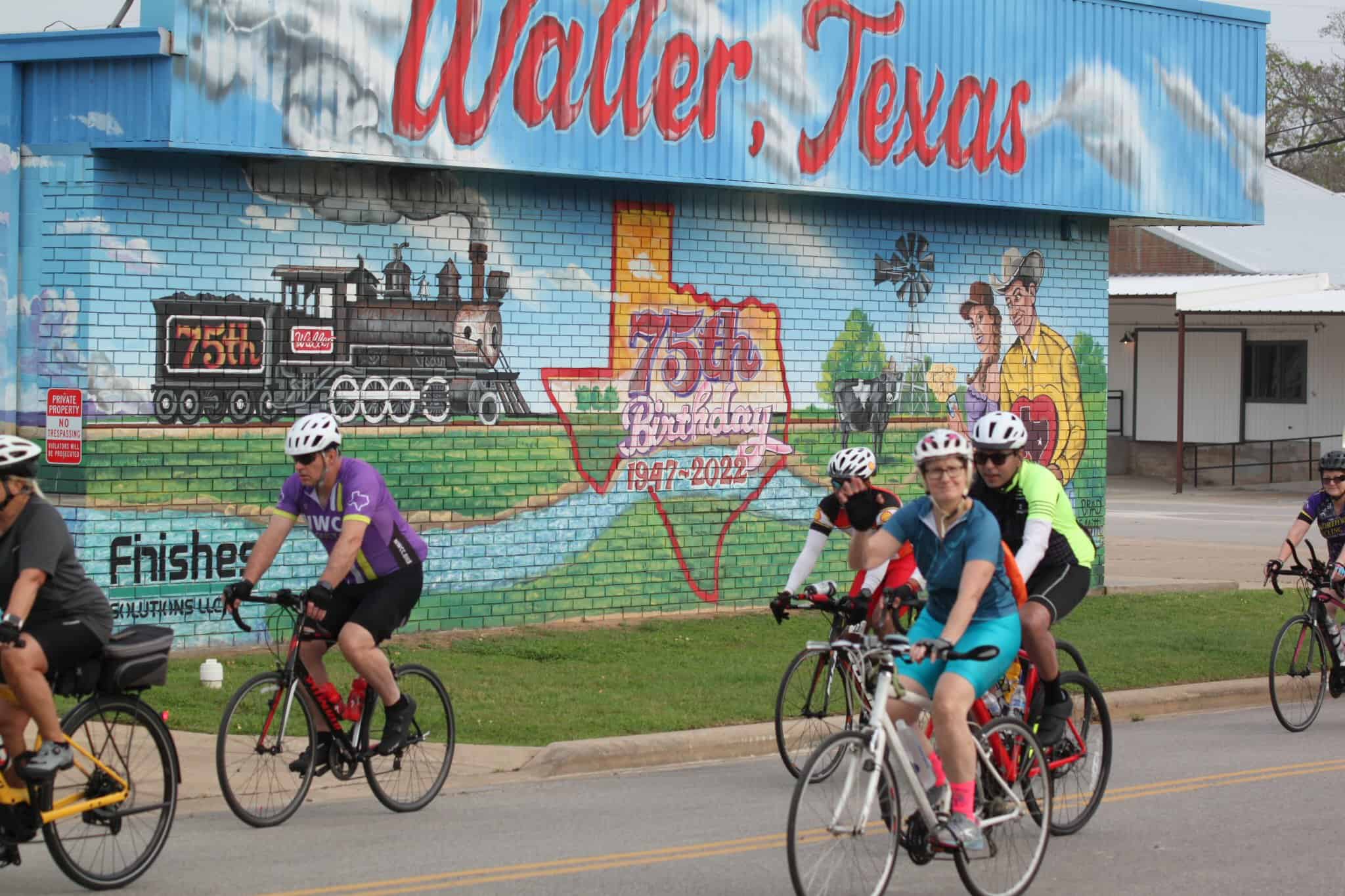 Colorful mural celebrating Bluebonnet Express's 75th birthday in Wallers, Texas, with cyclists riding past.