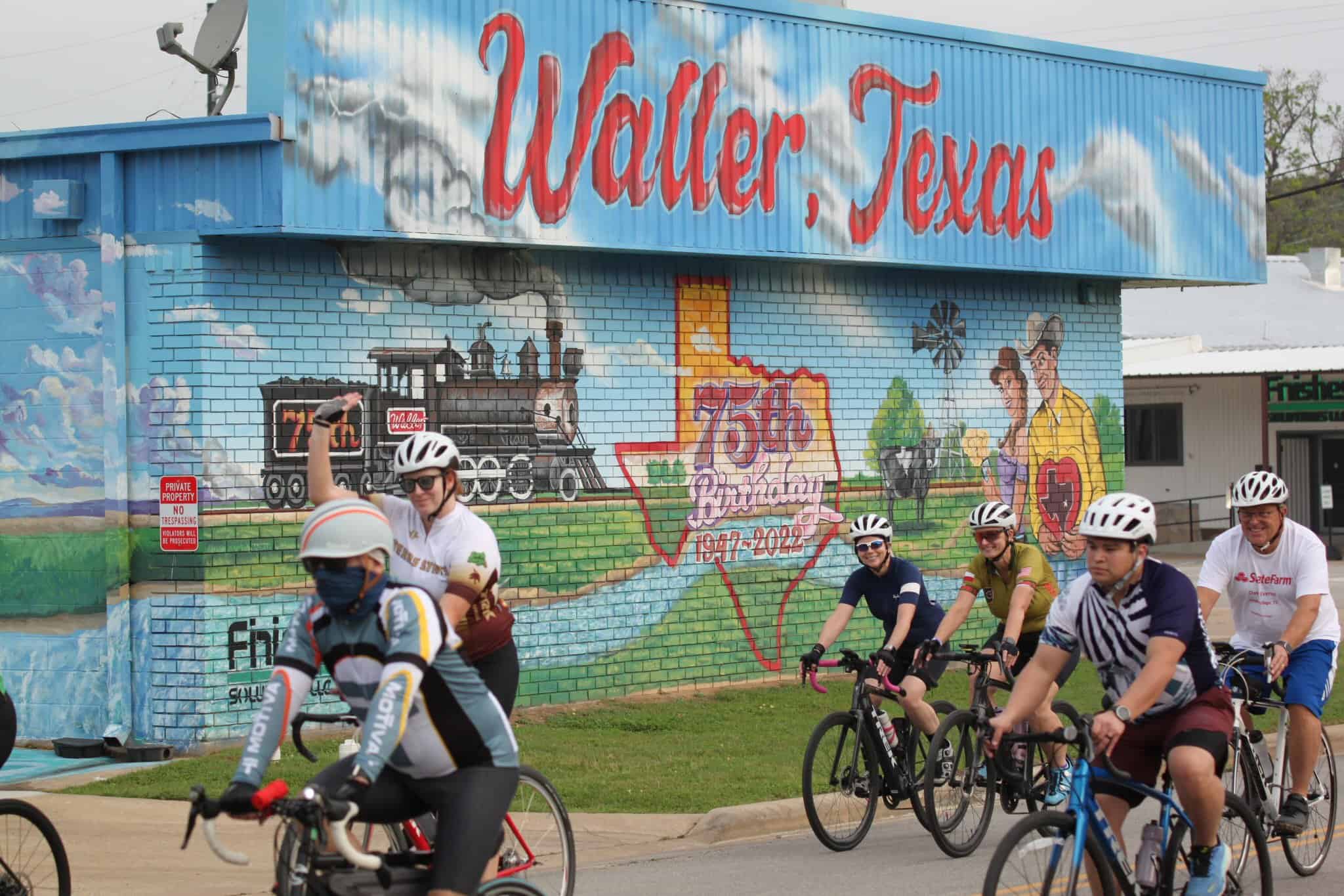 Colorful mural in Waller, Texas celebrating 75th anniversary with cyclists riding past.