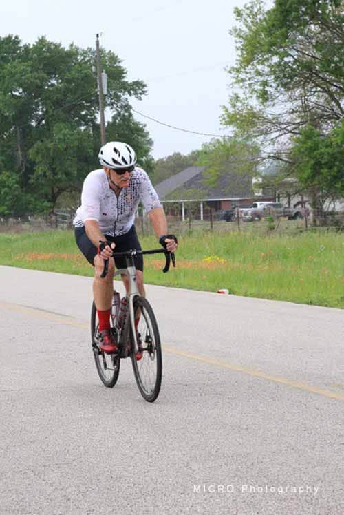Rider on a road bike wearing a helmet and cycling gear in a rural setting.