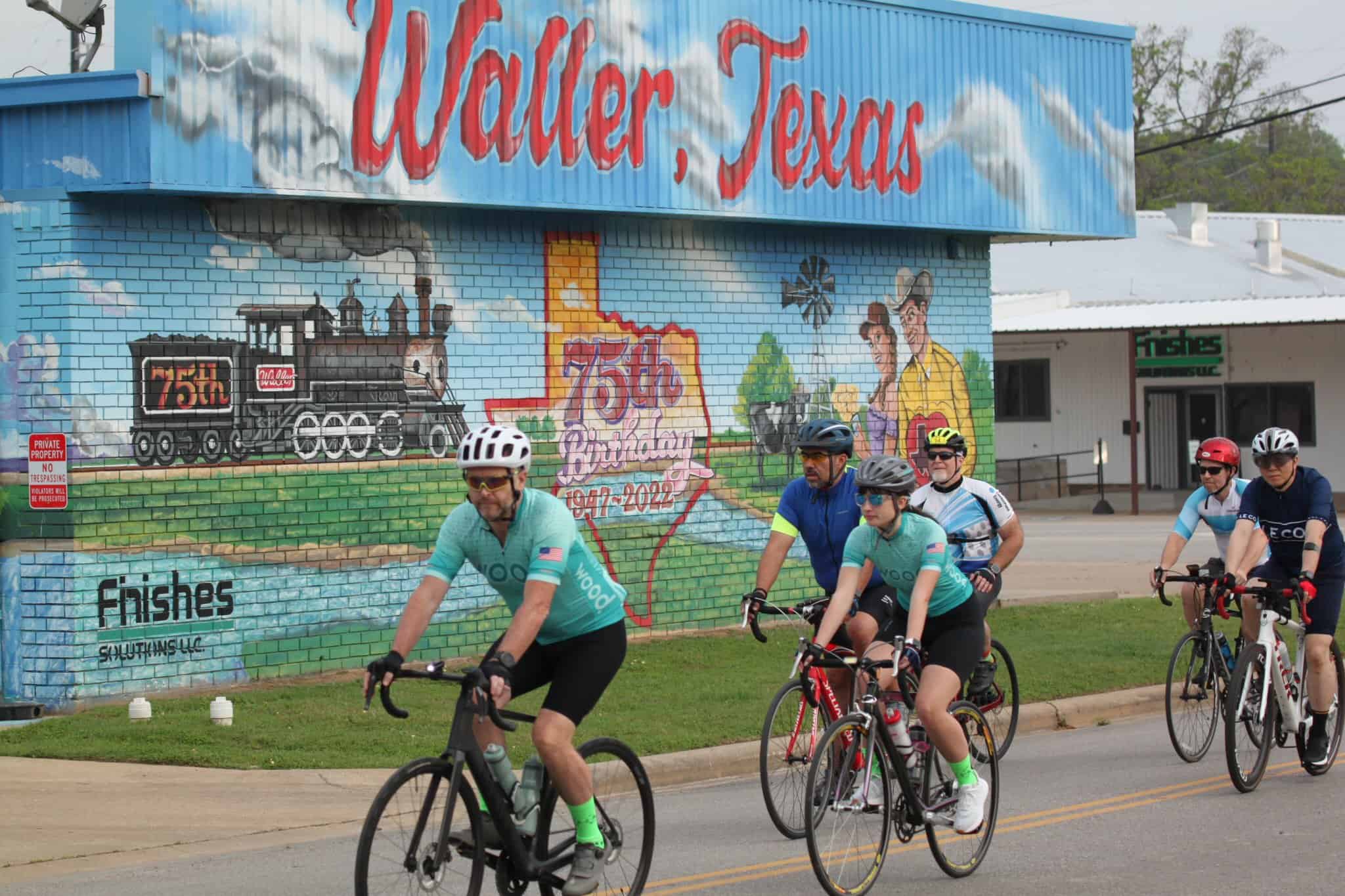 Brightly painted mural for Walker, Texas, celebrating Bluebonnet Express and 75th birthday. Cyclists ride past on a sunny day.