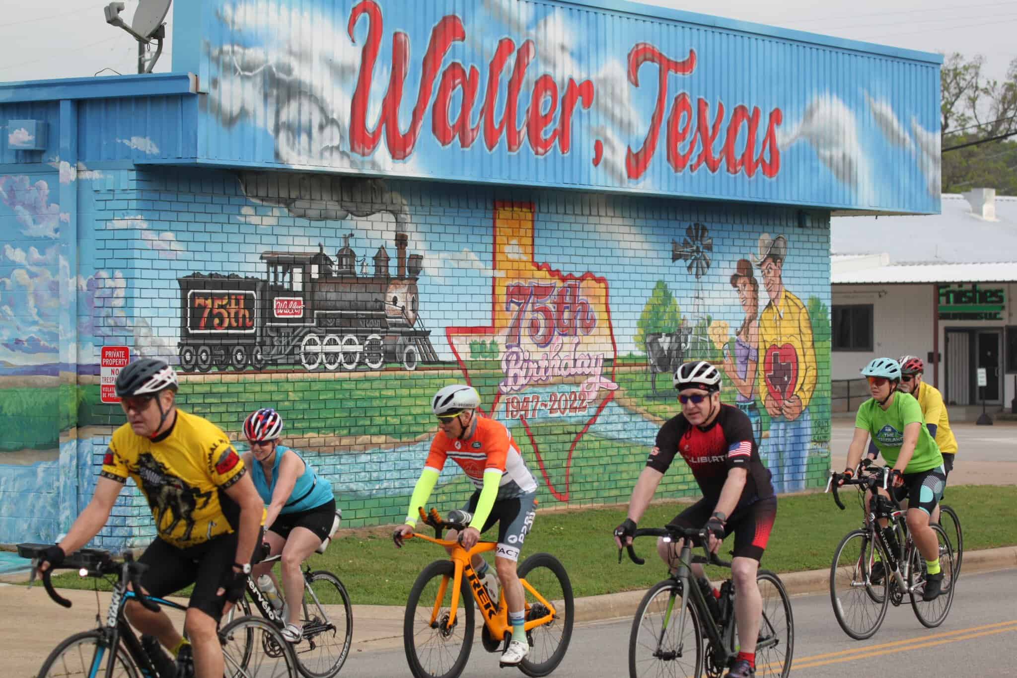 Colorful mural celebrating Waller, Texas 75th birthday with cyclists riding past.