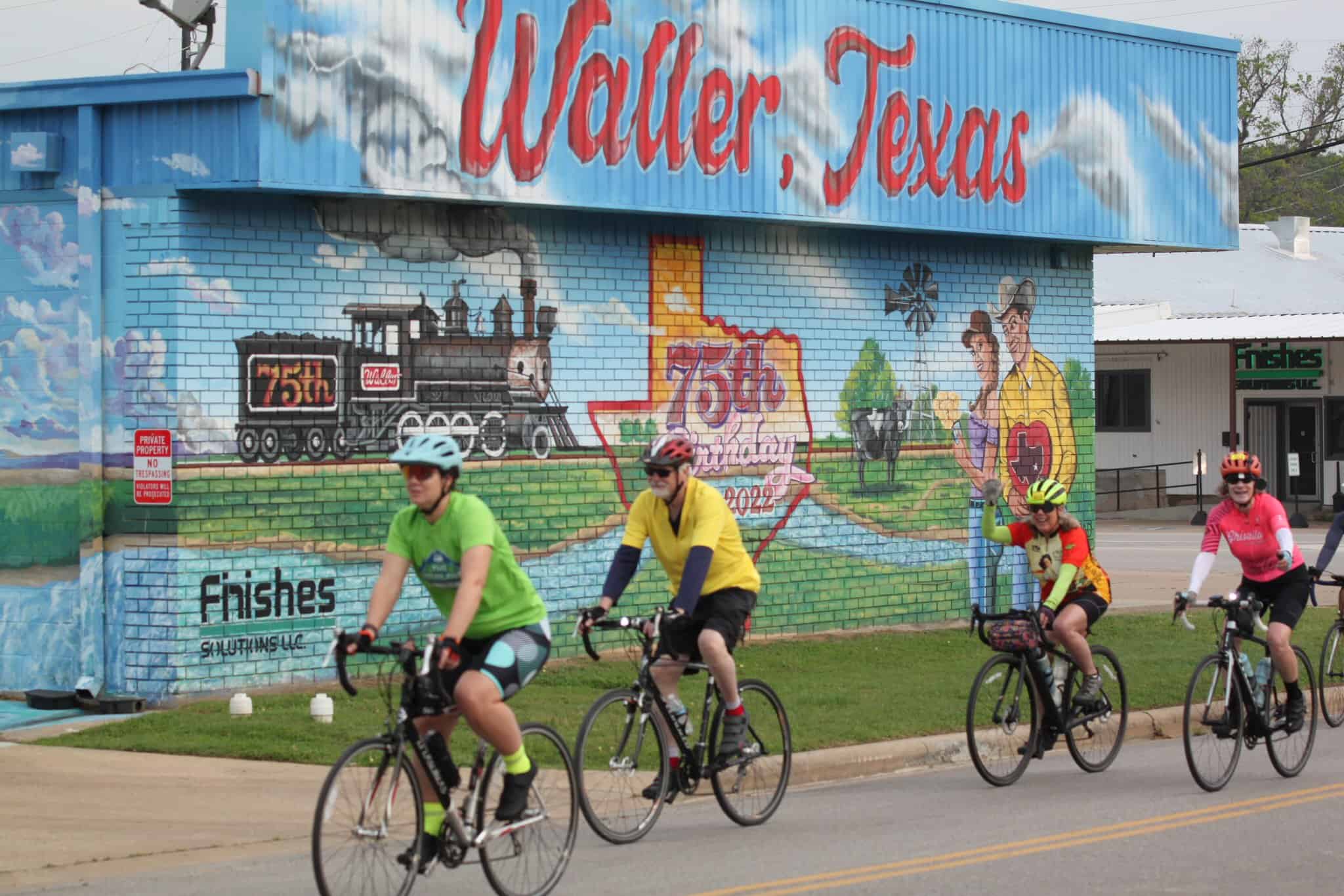 Colorful mural celebrating 75th anniversary of Walter, Texas, with cyclists riding past.