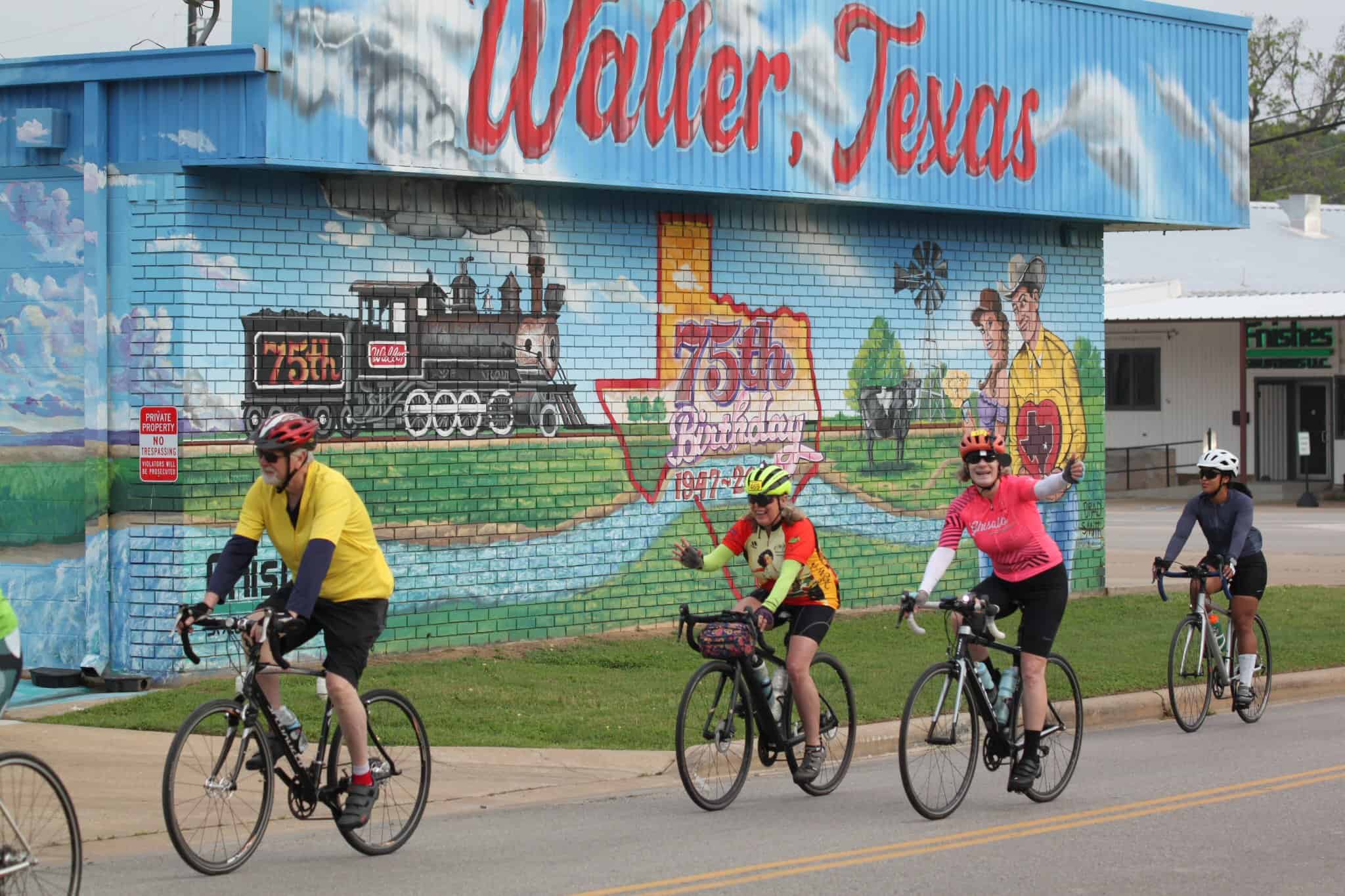 Brightly painted mural celebrating Waller, Texas, 75th anniversary with cyclists riding past.