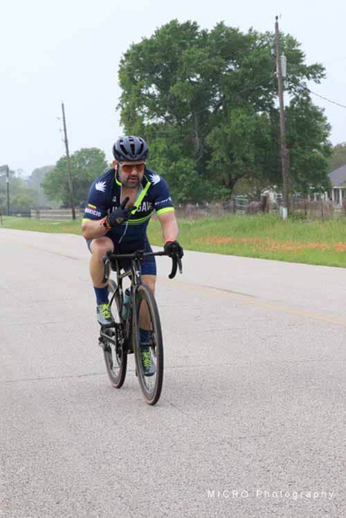 Cyclist riding on rural Texas street during daytime, promoting Bluebonnet Express bike event.