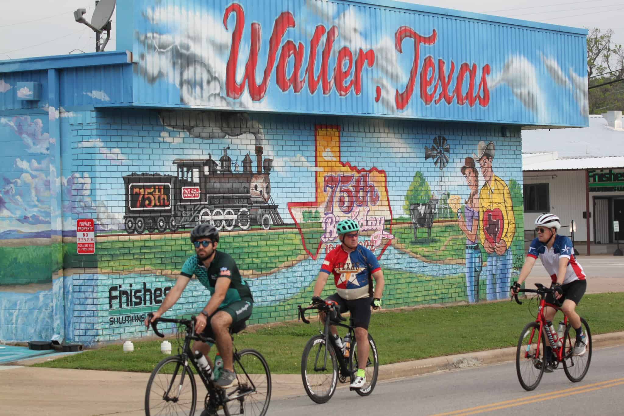 Colorful mural celebrating Wolf, Texas, 75th anniversary with cyclists passing by.