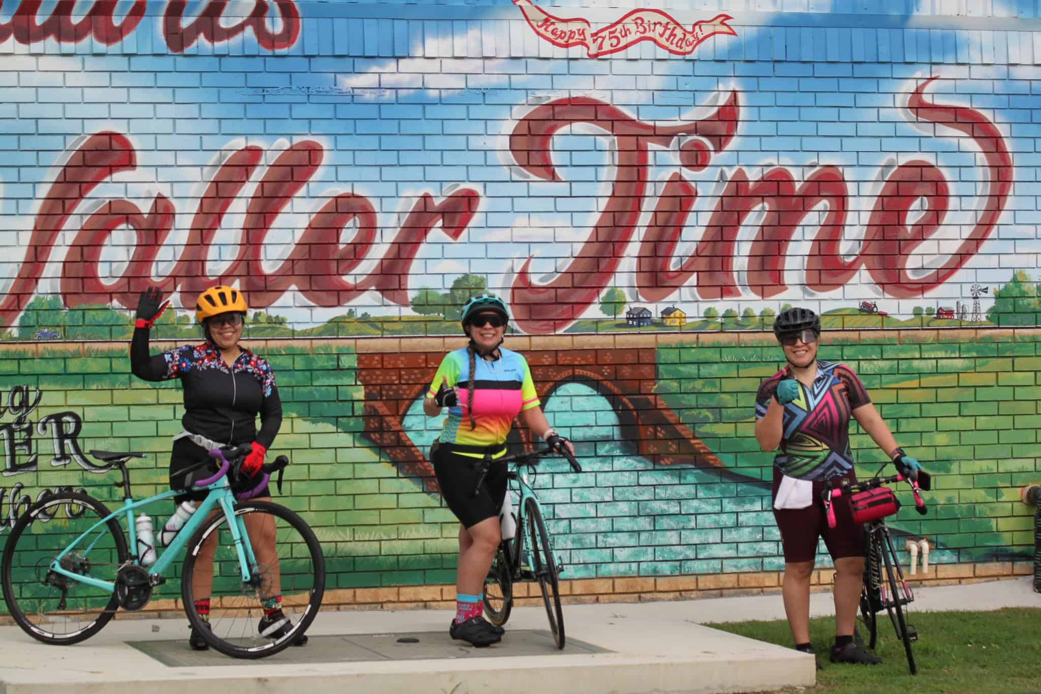 Colorful cyclists at Bluebonnet Express mural, celebrating bike ride event and community.