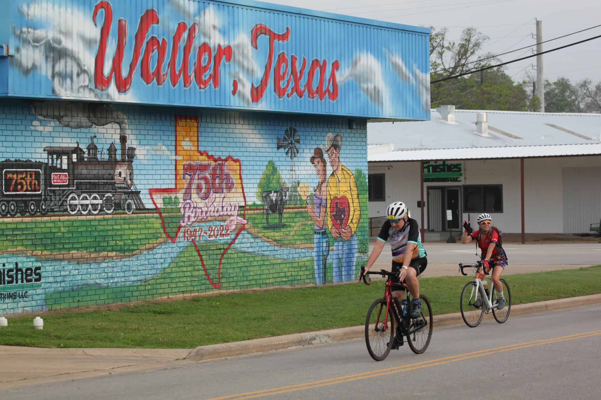 Bright mural celebrating Wallers, Texas 75th anniversary with cyclists riding past.