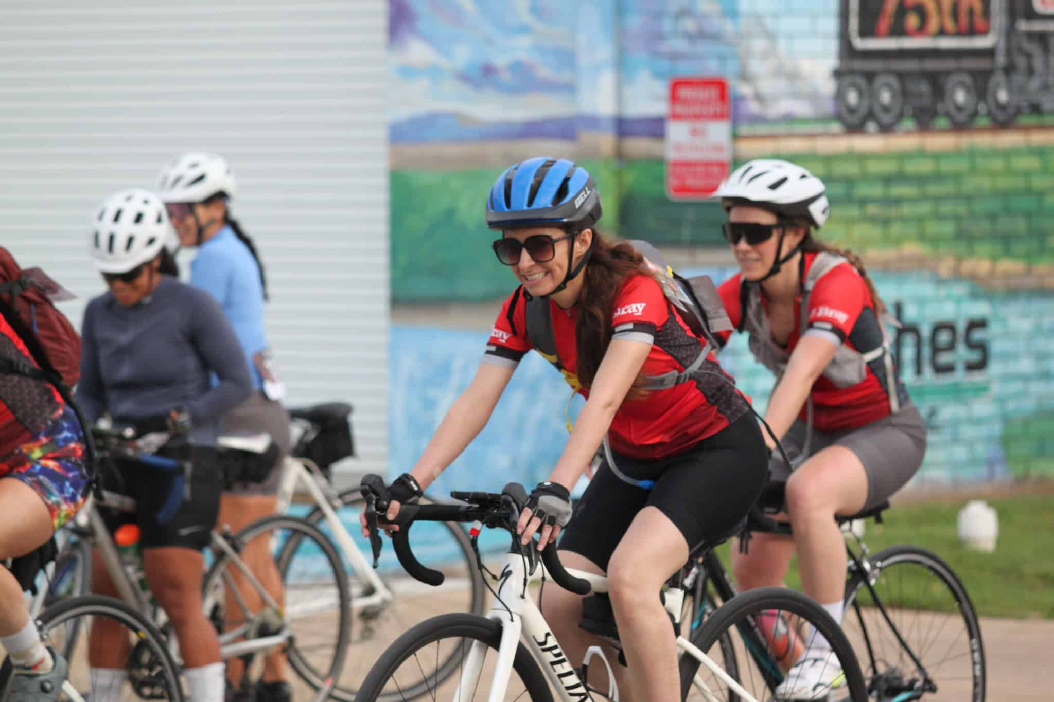 Bright female cyclist smiling on Bluebonnet Express bike ride, wearing safety gear and stylish sunglasses.