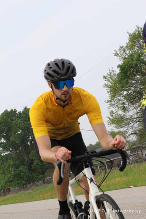 Bright cyclist in yellow jersey and black helmet riding a road bike outdoors on a cloudy day.