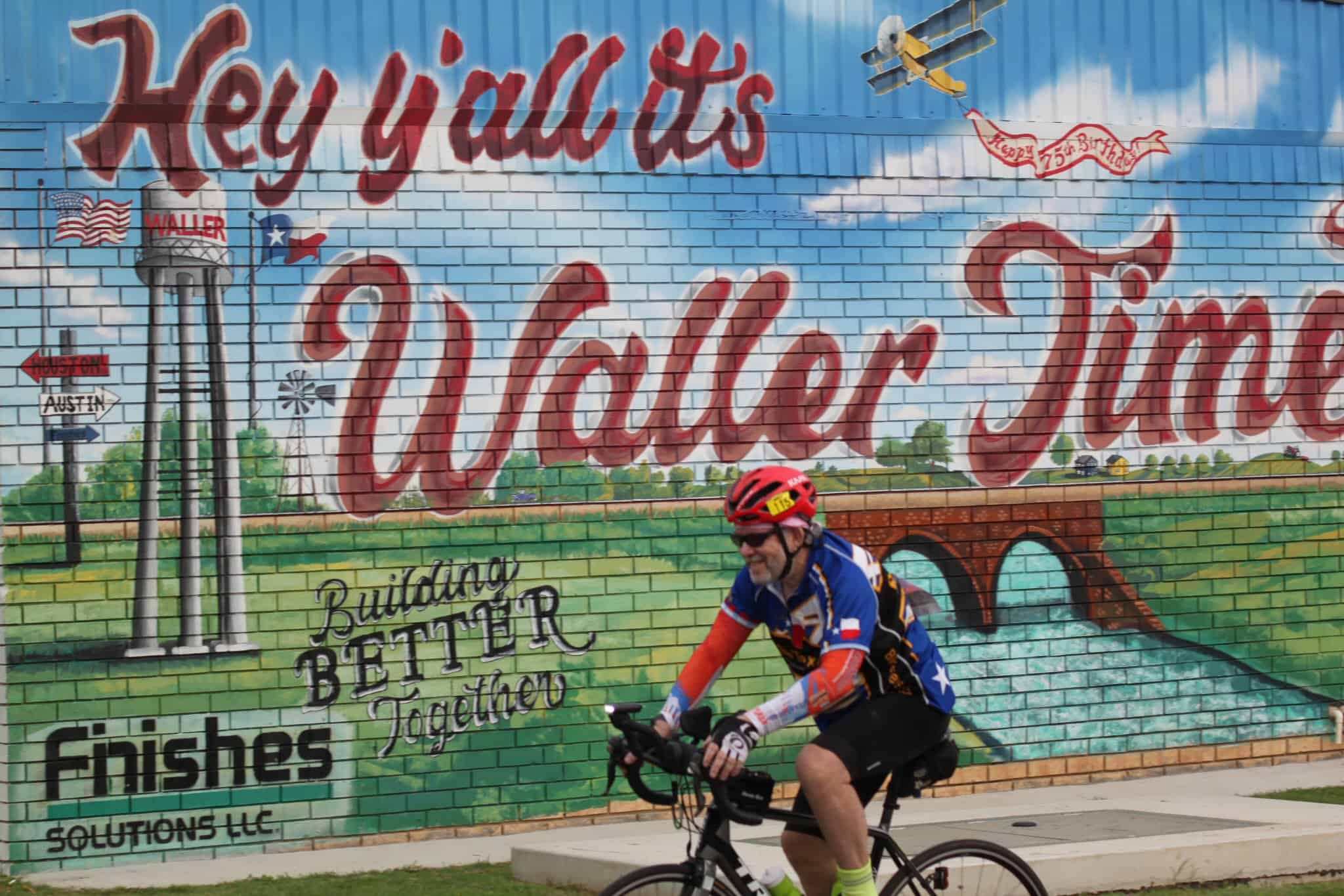 Colorful mural of Waller, Texas with cyclist in front, highlighting local landmarks and community spirit.
