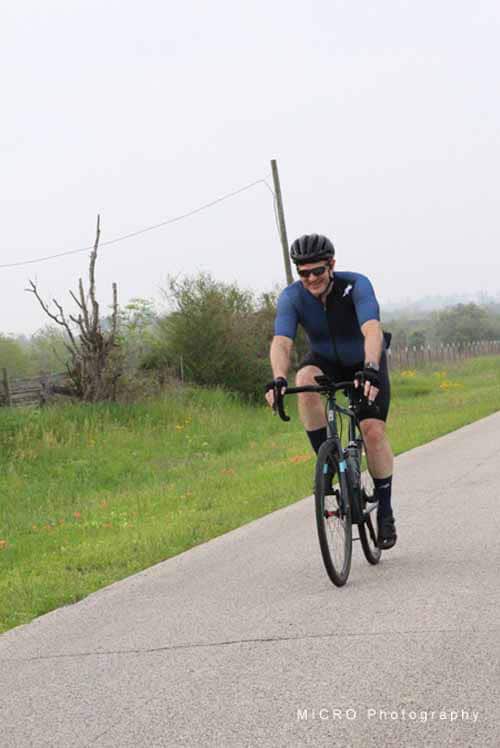 Brightly dressed cyclist riding on a scenic outdoor trail with greenery and overcast sky.