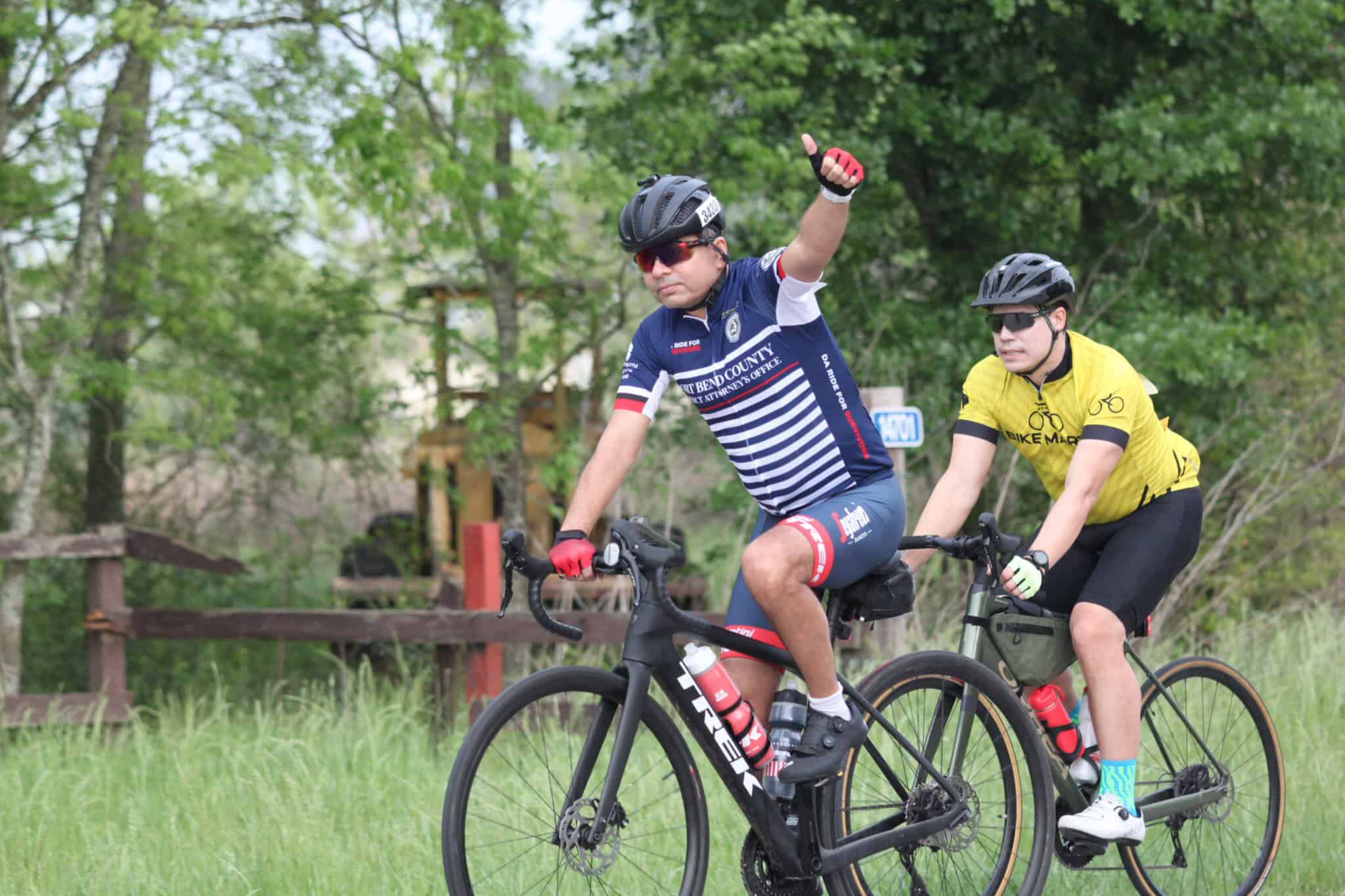 Bright blue and yellow cycling jerseys on two cyclists during Bluebonnet Express event in lush green outdoor setting.