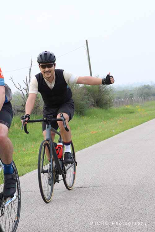 - Bicycle rider smiling giving a thumbs-up during a scenic cycling ride outdoors.