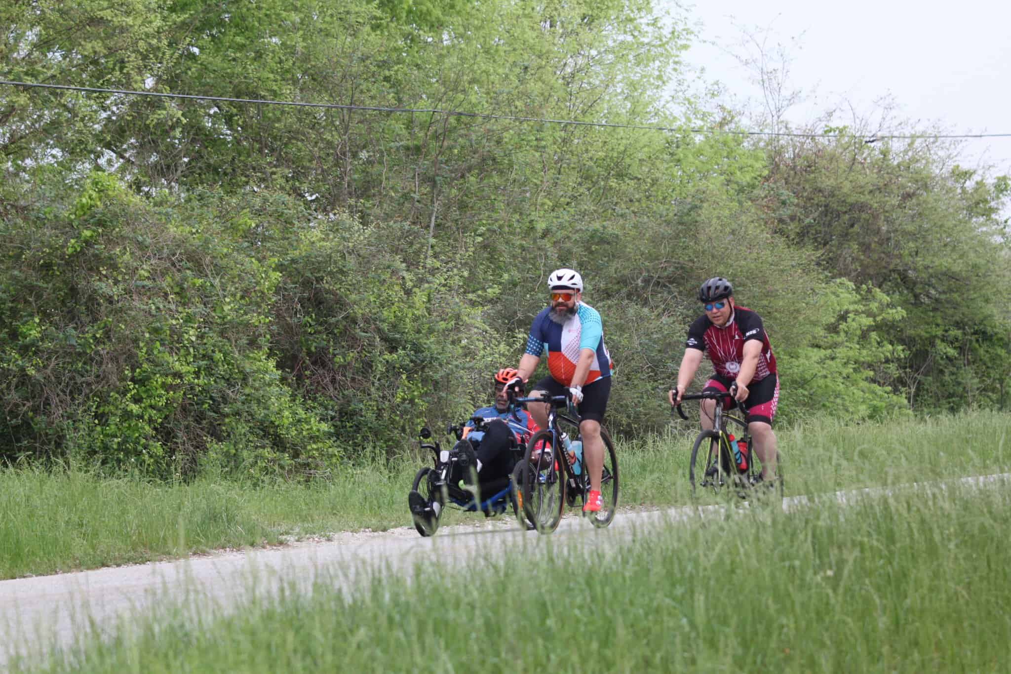 Bright blue and red bikes on scenic trail with cyclists and green trees.
