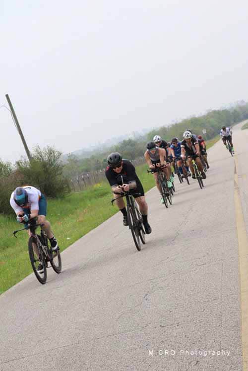 High school cyclists riding together on rural road during Bluebonnet Express event.