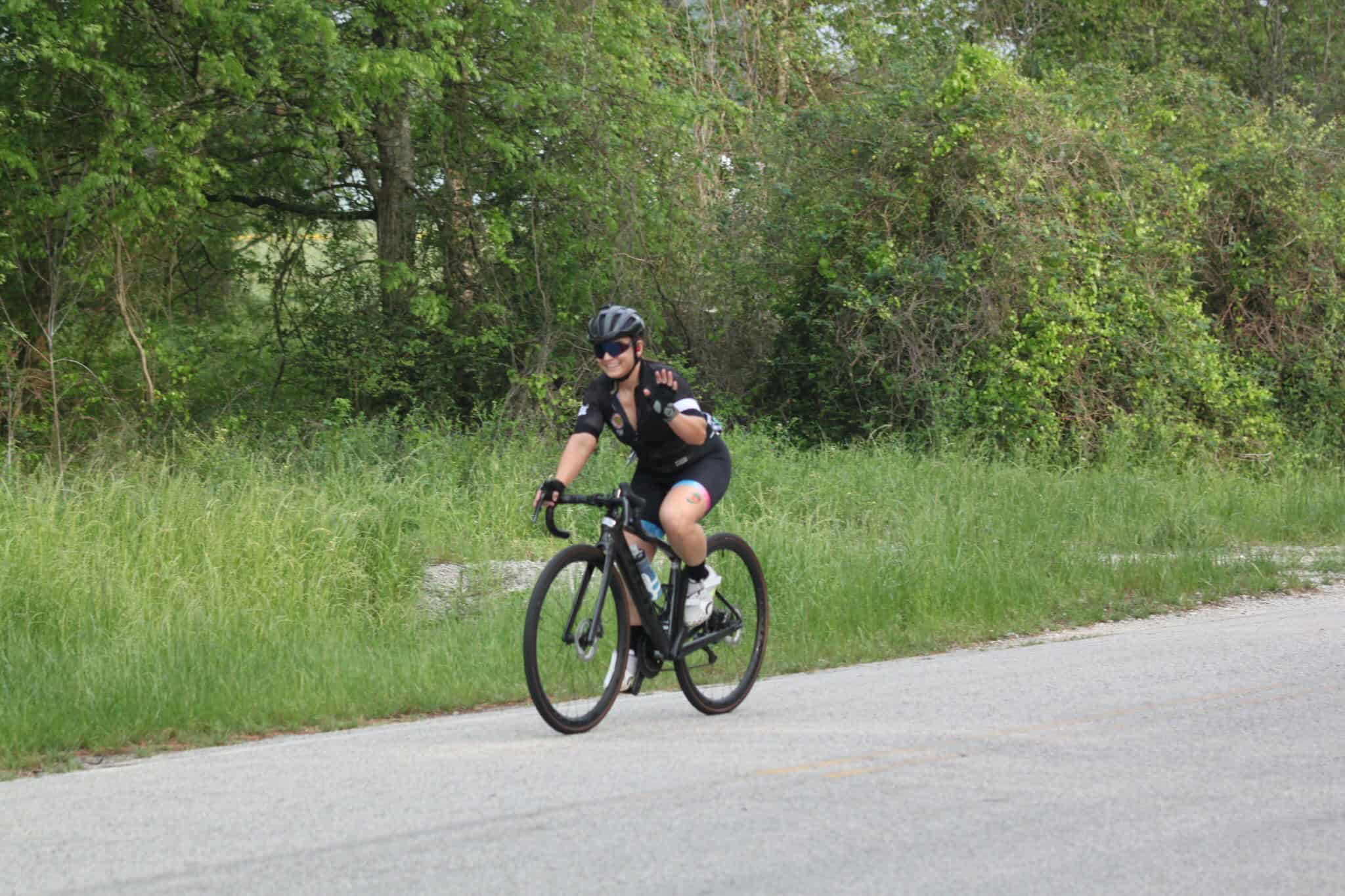 Vibrant cyclist riding a black road bike on scenic trail with lush greenery for Bluebonnet Express.