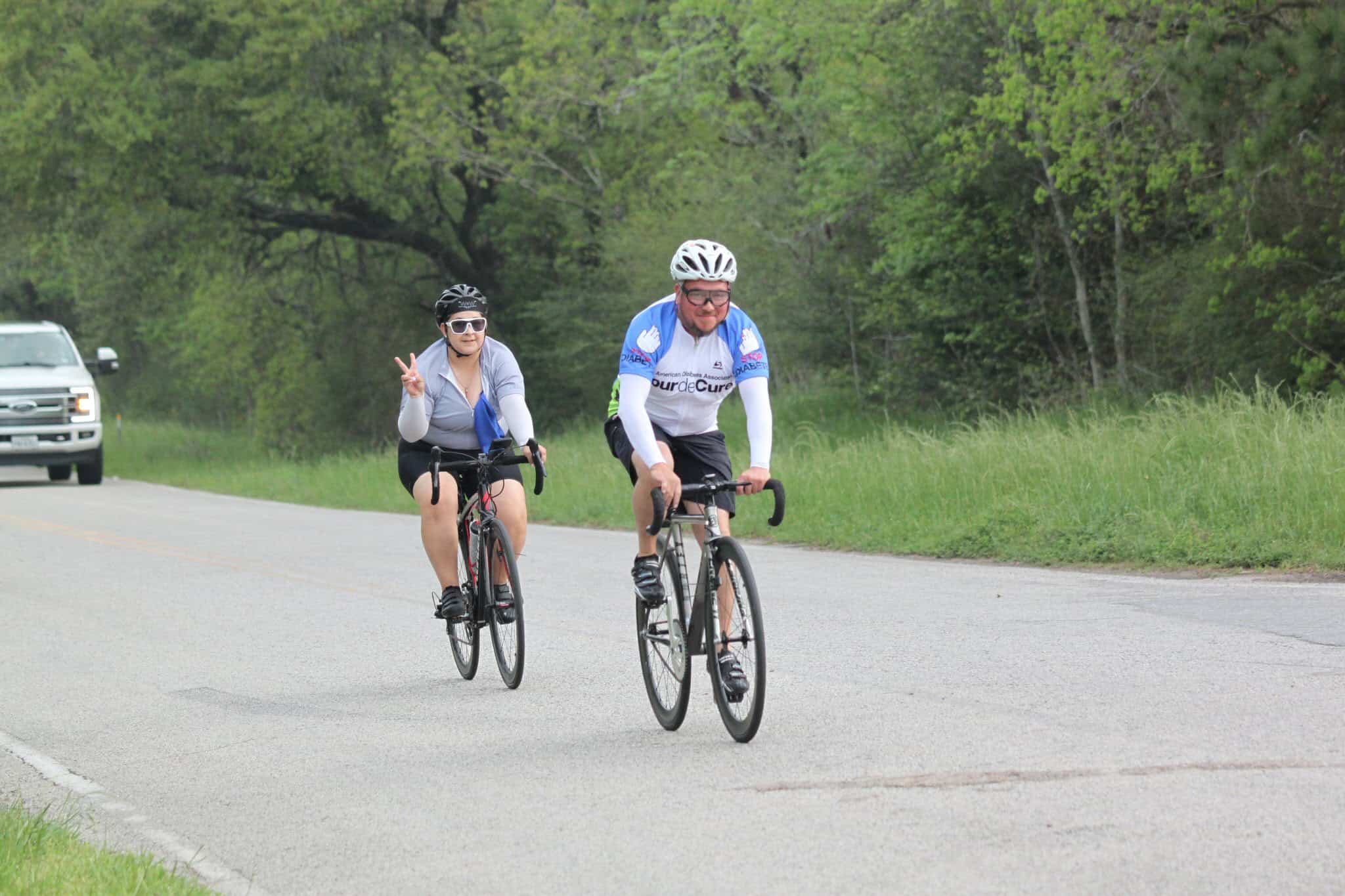 Bright, cheerful cyclists enjoying scenic bike ride on rural road with lush green trees in background.