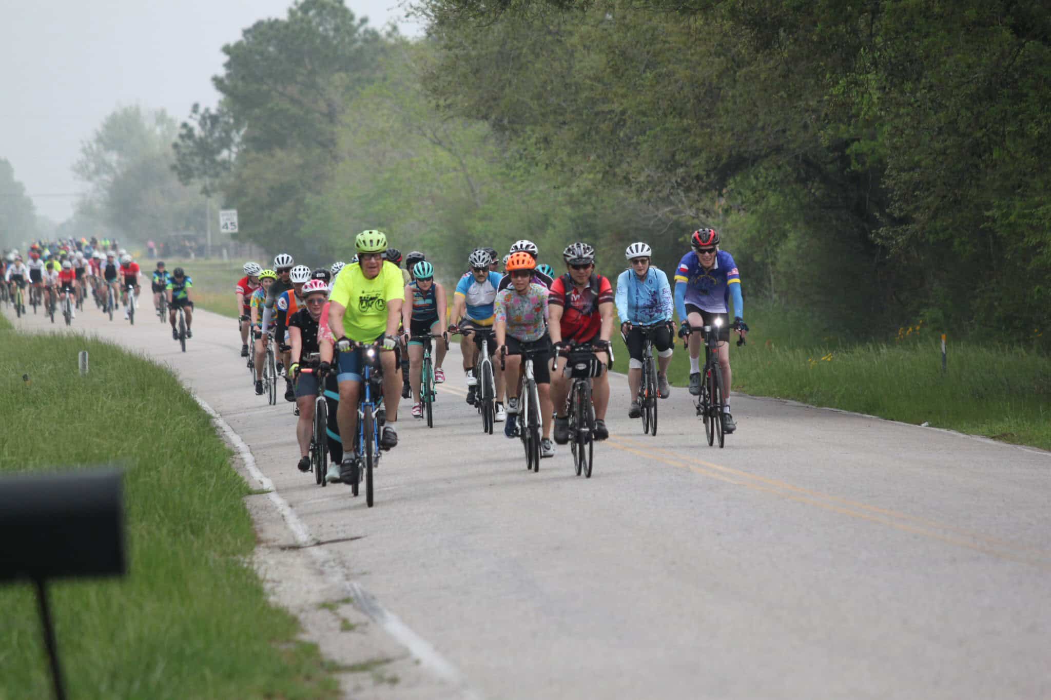 Cyclists riding on a rural road during a group bike race or fun ride in outdoor nature setting.