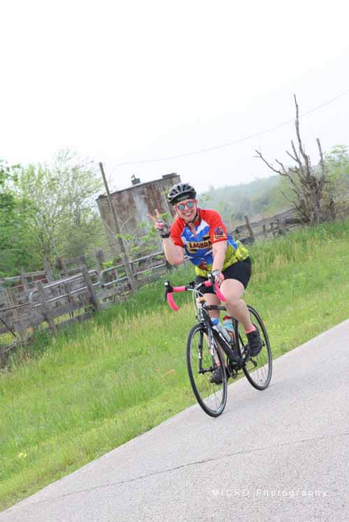 Bright woman cycling on scenic rural road with bicycle and helmet, enjoying outdoor biking adventure.