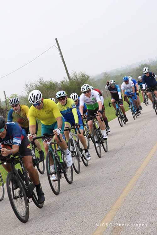 Vibrant group of cyclists riding together on a scenic road during Bluebonnet Express event.