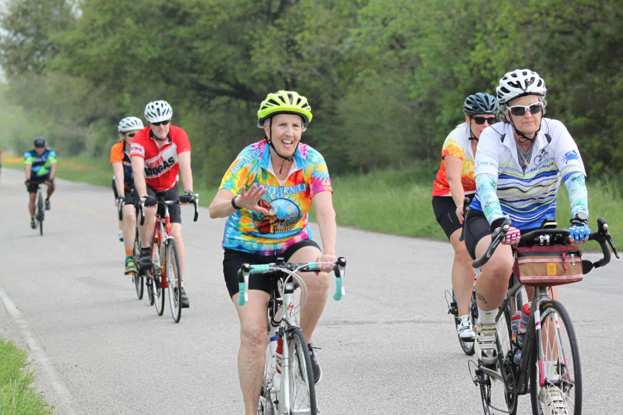 Colorful cyclists riding along scenic road for Bluebonnet Express event.