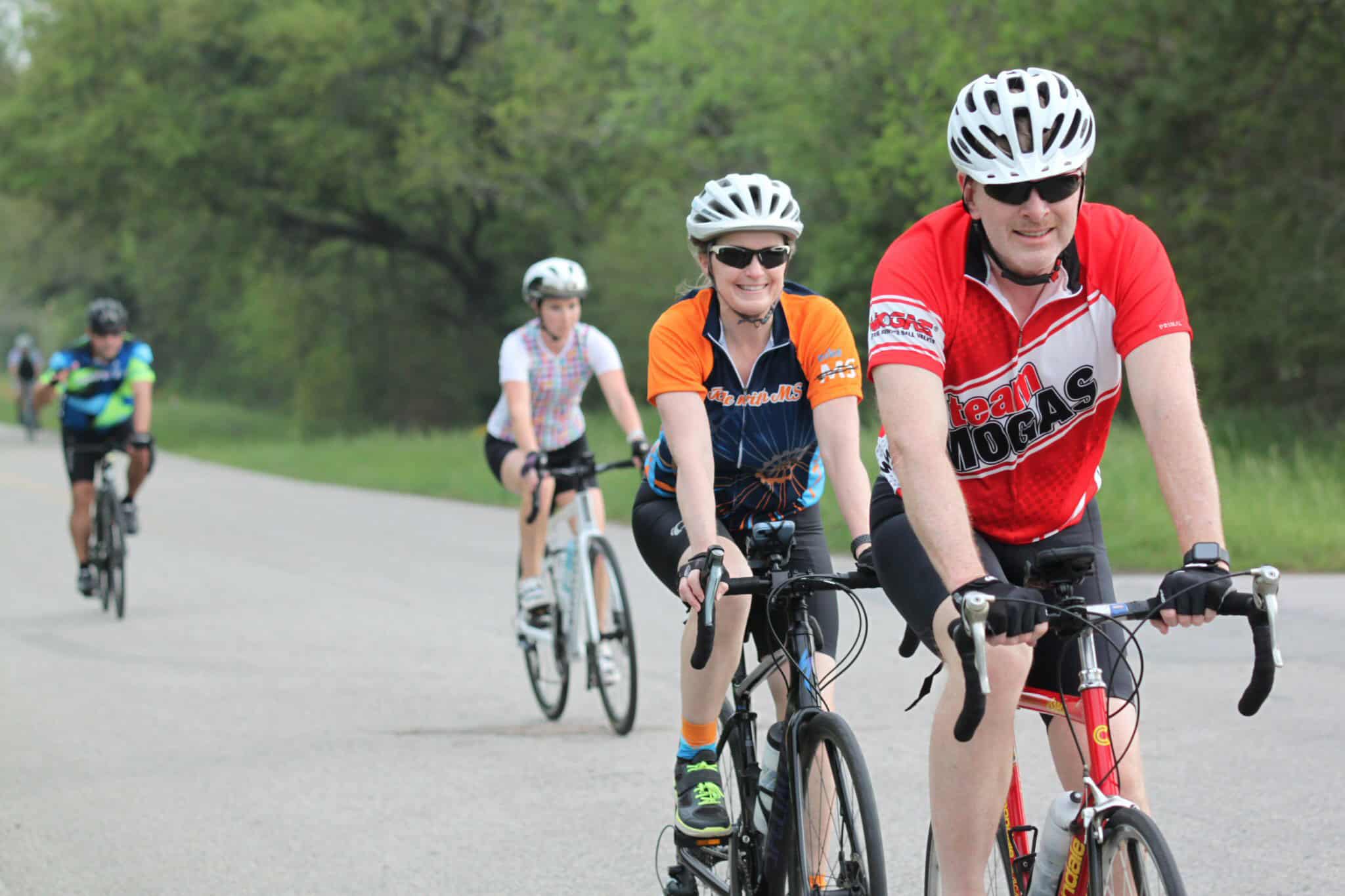 Vibrant group of cyclists riding through scenic green landscape on Bluebonnet Express trail.