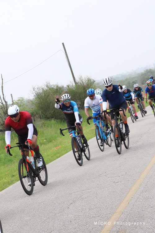 Bright Bluebonnet Express cycling team riding on rural road in Texas, supporting bike events and outdoor adventures.
