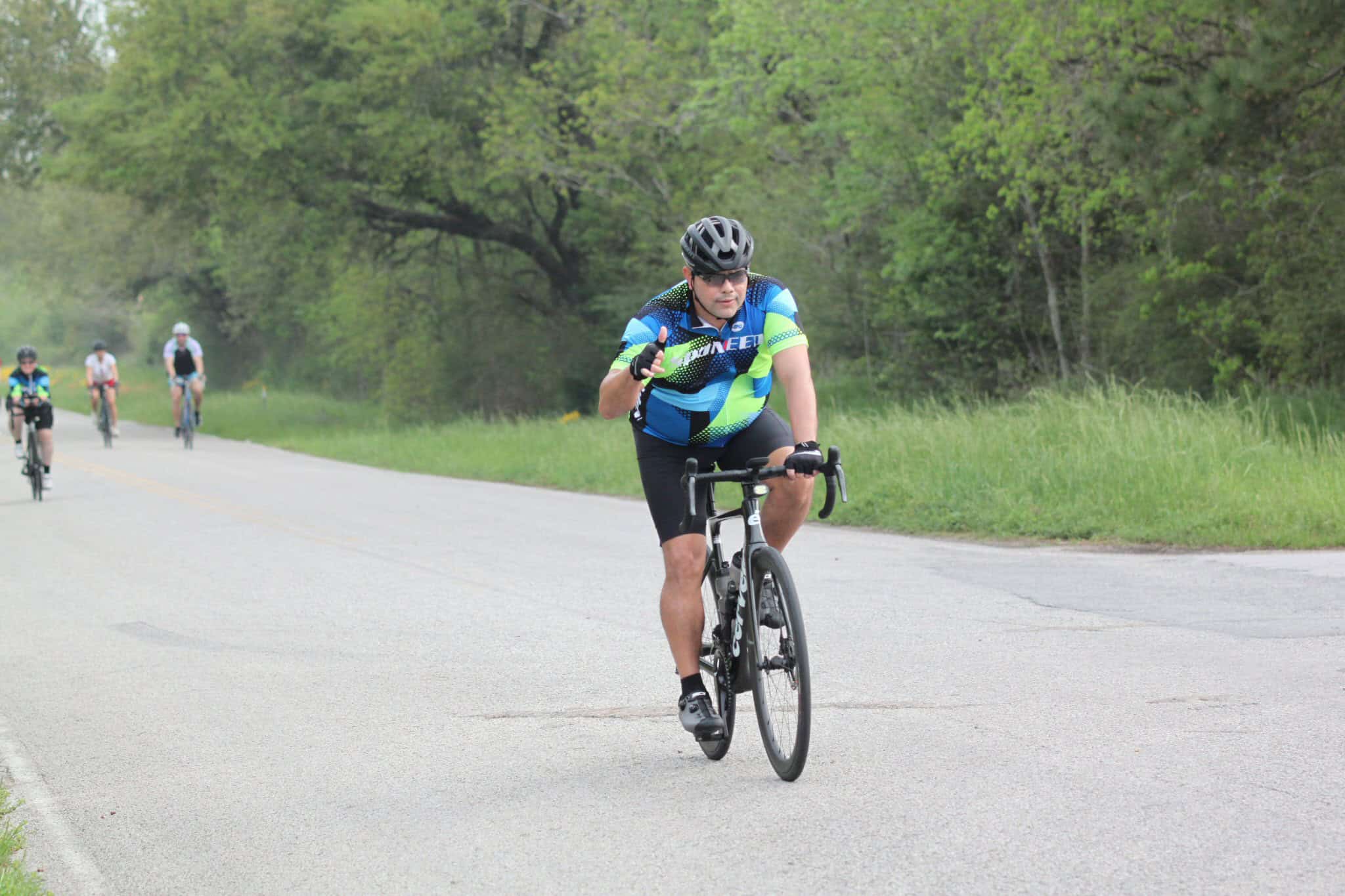 High-performance cyclist riding on scenic country road with lush green trees, promoting Bluebonnet Express bike tours.