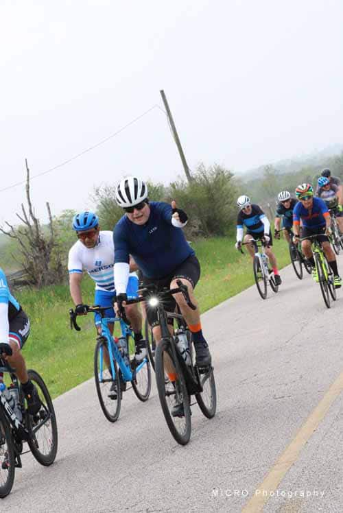 Bright group of cyclists riding on a scenic road during Bluebonnet Express event in Texas.