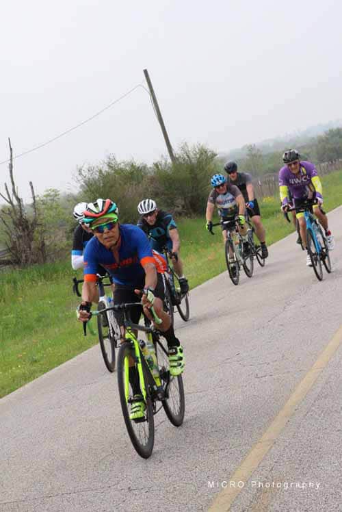Riders on bikes during Bluebonnet Express cycling event on scenic rural road.