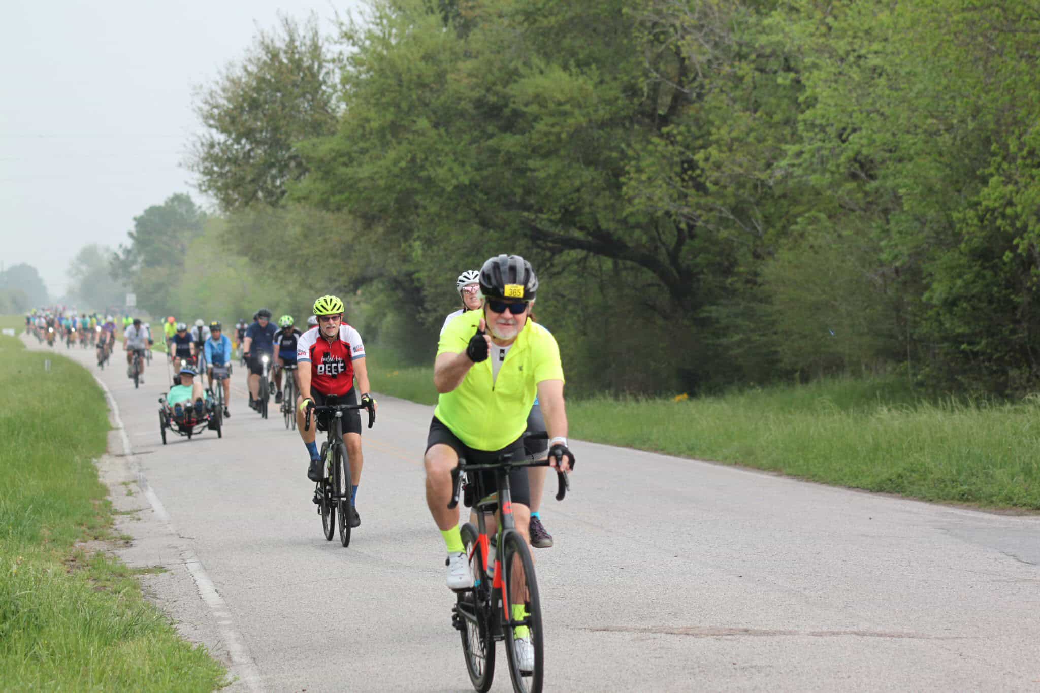 Bright yellow cycling jersey and helmet at Bluebonnet Express bike race with group of riders along scenic green route.