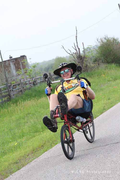 Bright yellow cyclist shirt, outdoor riding on a recumbent tricycle with scenic greenery.