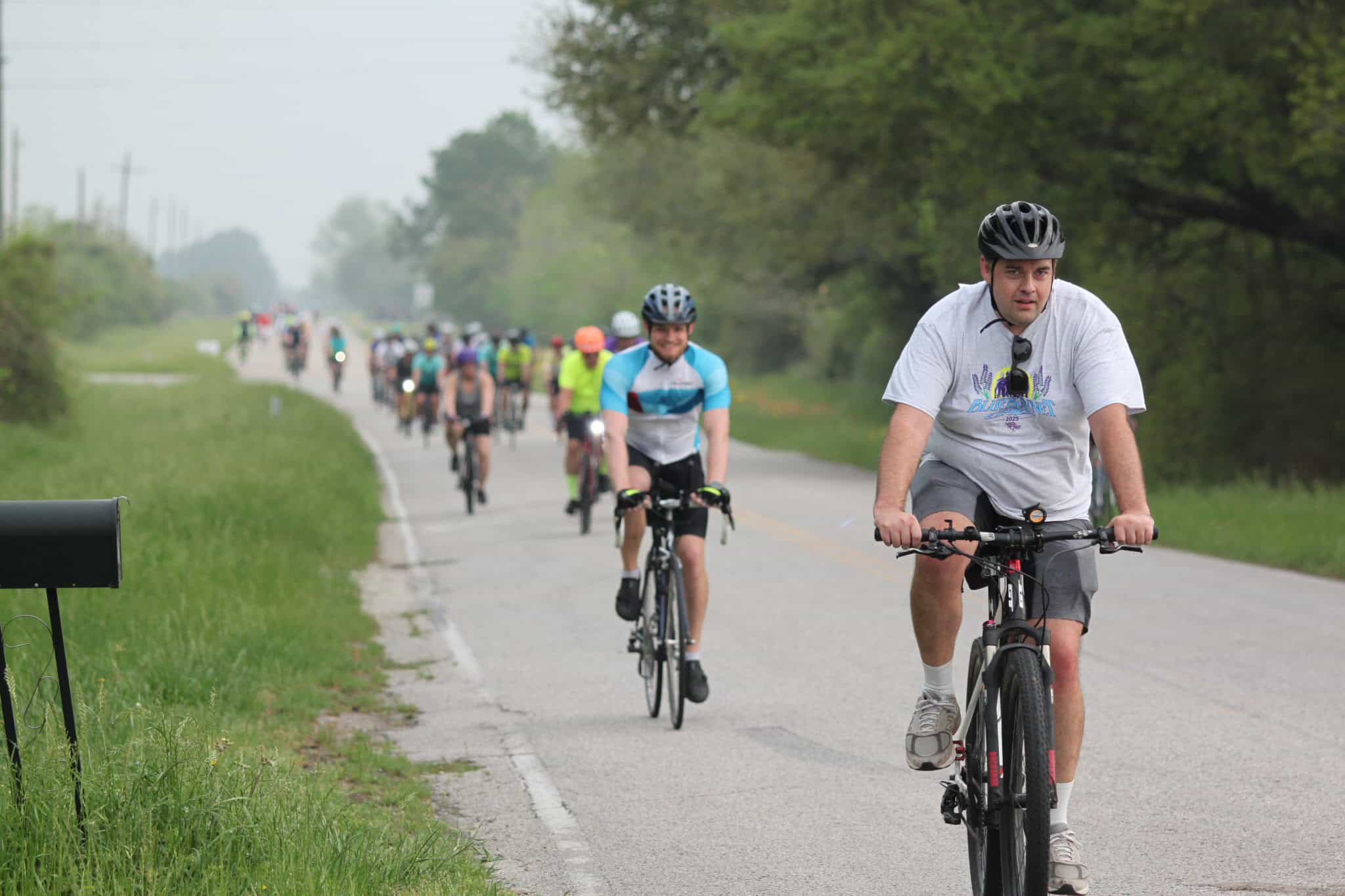 Brightly colored cyclists riding along a scenic rural road at the Bluebonnet Express event.