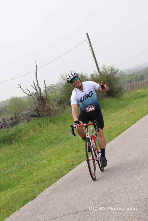 Bike rider in UBG cycling jersey on rural road during Bluebonnet Express event, enjoying scenic spring ride.