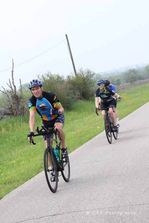 Brightly dressed cyclists riding on a scenic rural road during daytime, promoting outdoor biking adventures.