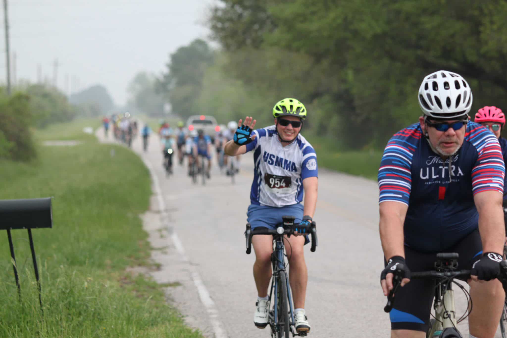 Brightly colored cyclist waving during Bluebonnet Express cycling event in Texas, surrounded by lush greenery.