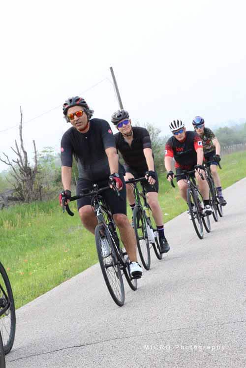 Small group of cyclists riding on a scenic bike trail during daytime, promoting Bluebonnet Express bicycle event.