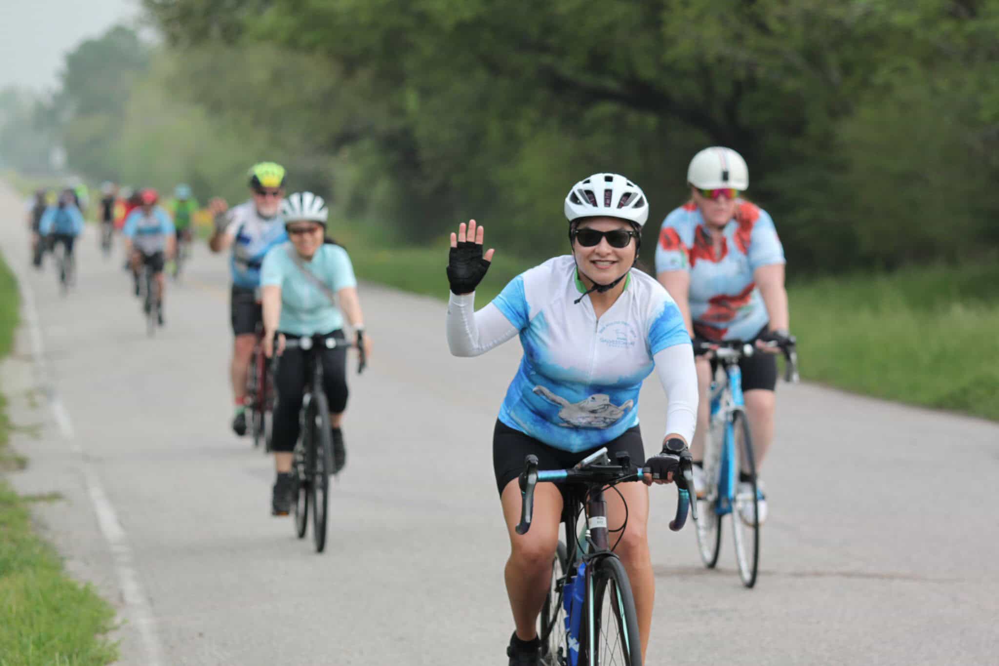 Bright female cyclist waving while riding with a group on a scenic bike route.