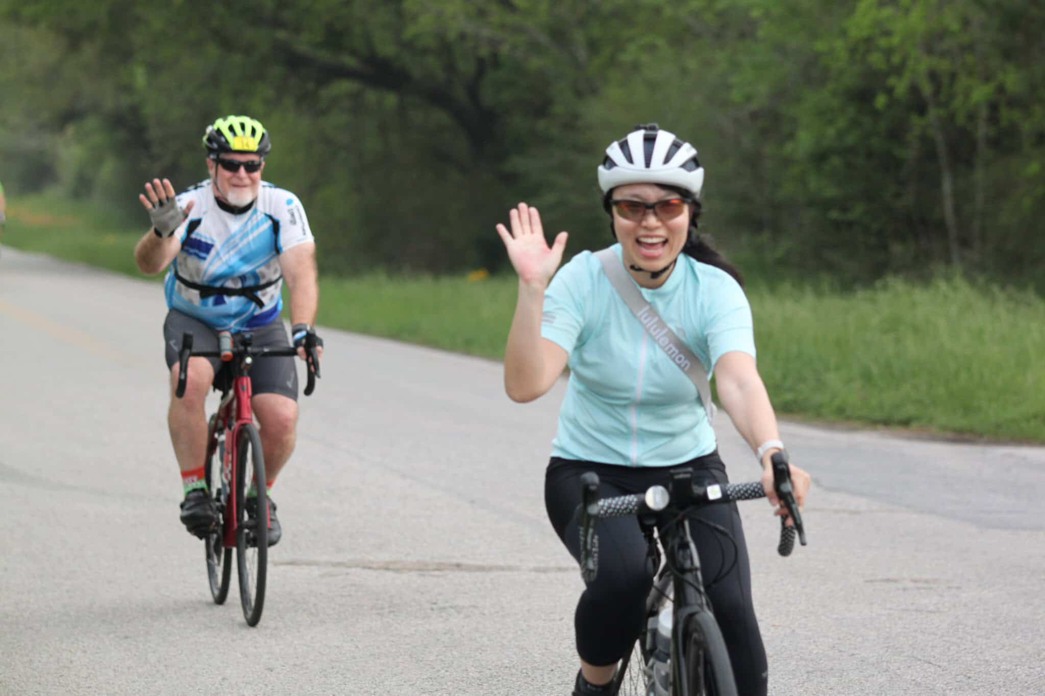 Happy cyclists waving on scenic road for Bluebonnet Express bike event.