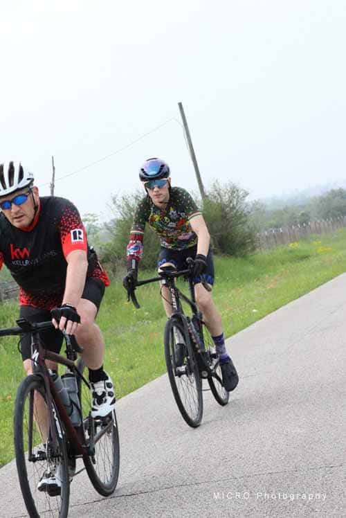 Vibrant cyclists riding on a scenic rural road during daytime, promoting outdoor cycling events.