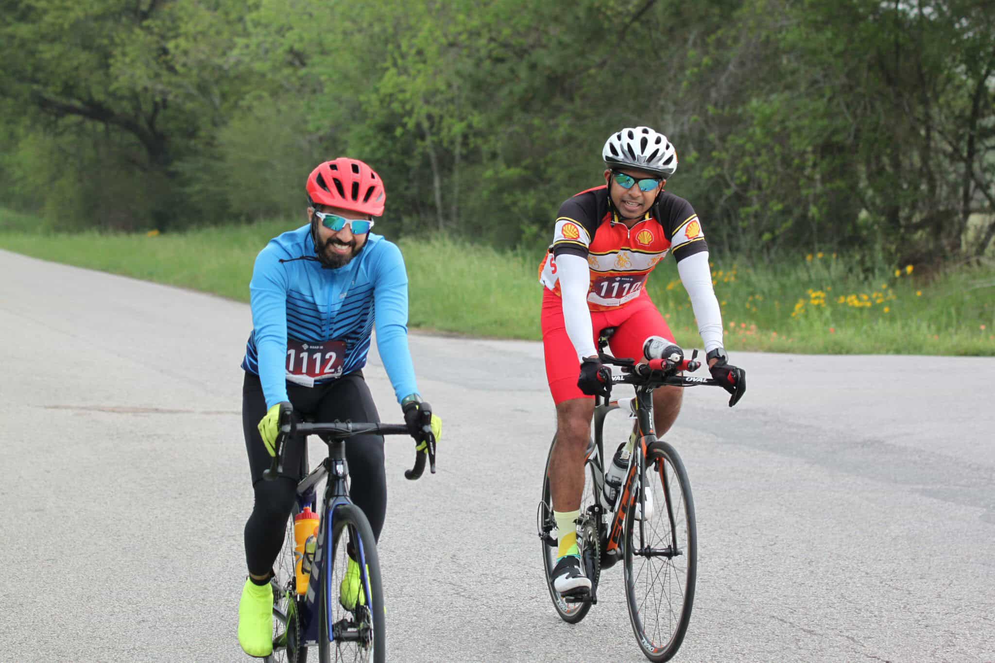 Vibrant cyclists riding on a scenic open road surrounded by greenery and wildflowers.